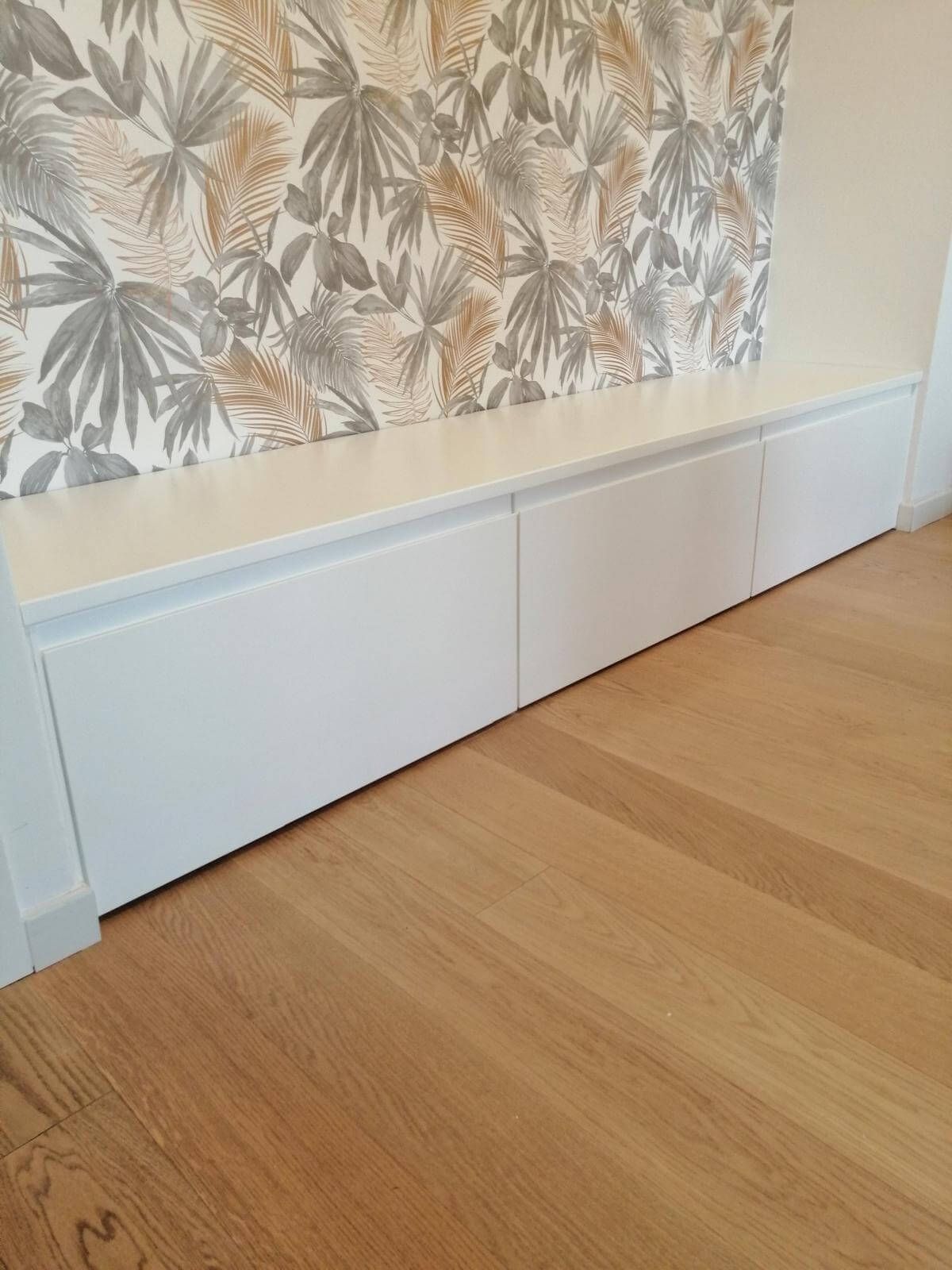 Un pavimento in legno e un mobile bianco in un soggiorno con una carta da parati floreale sulla parete.