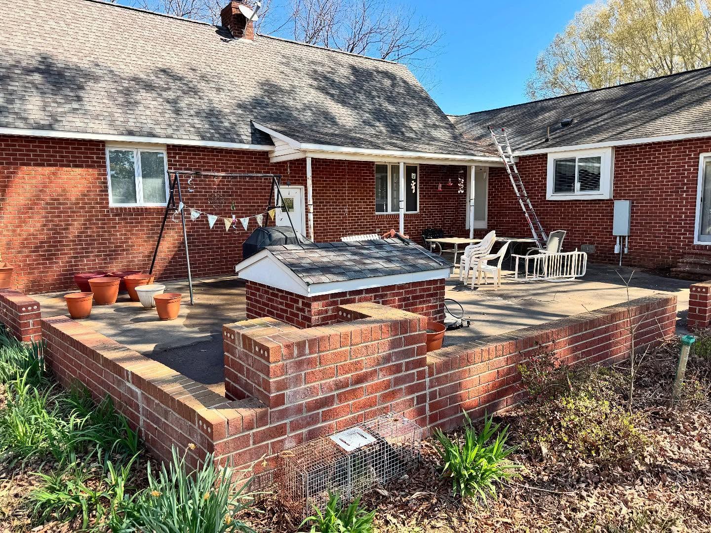 Red brick house with a patio, flower pots, and outdoor furniture. A ladder leans against the house.