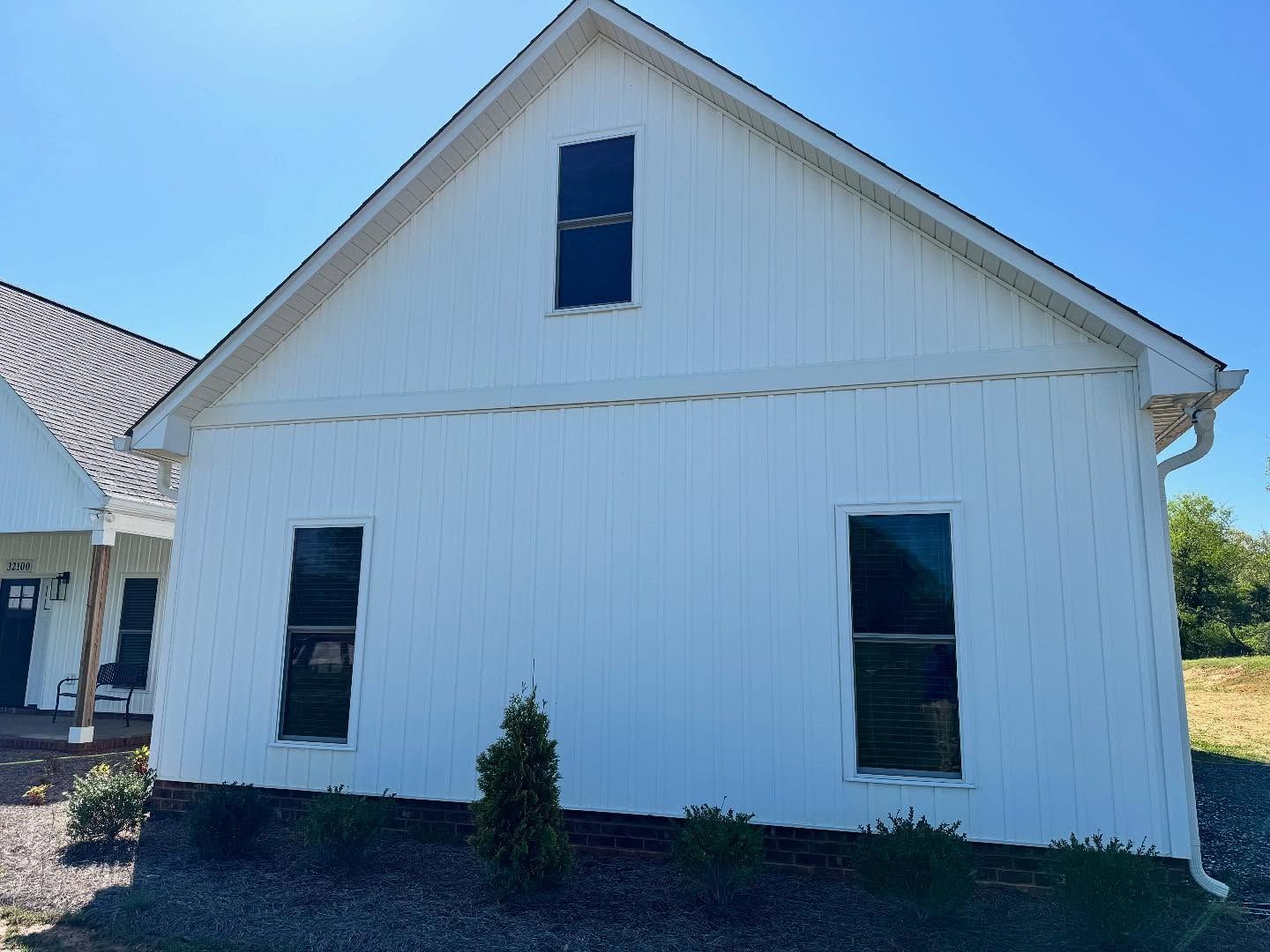 White house with vertical siding, three dark windows, and a blue sky.