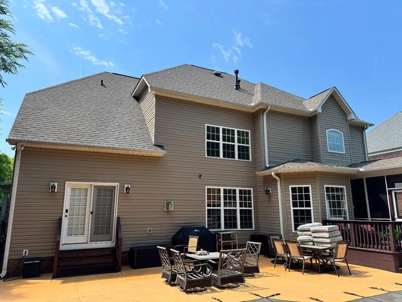 Back view of a two-story house with brown siding, a brown roof, and a patio area with outdoor furniture.