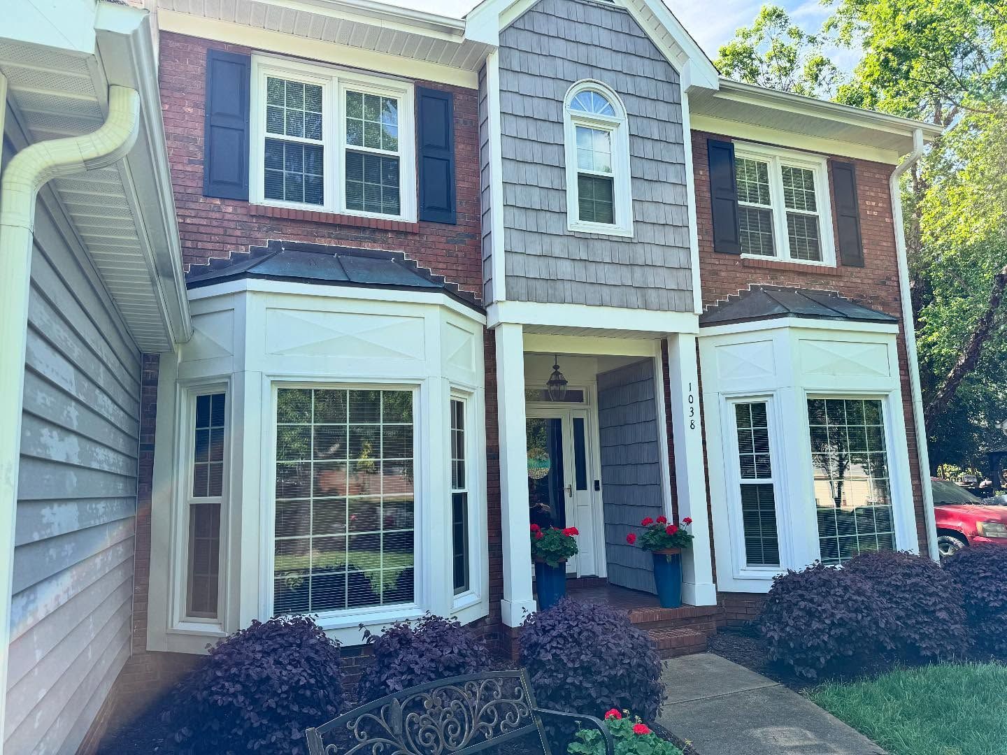 Two-story brick house with bay windows, gray siding, and a front entrance. Red brick contrasts with white trim and bla