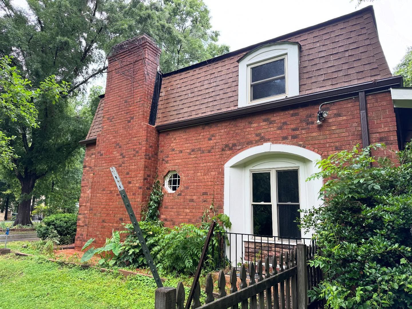 Red brick house with a steeply pitched roof, chimney, and arched doorwa