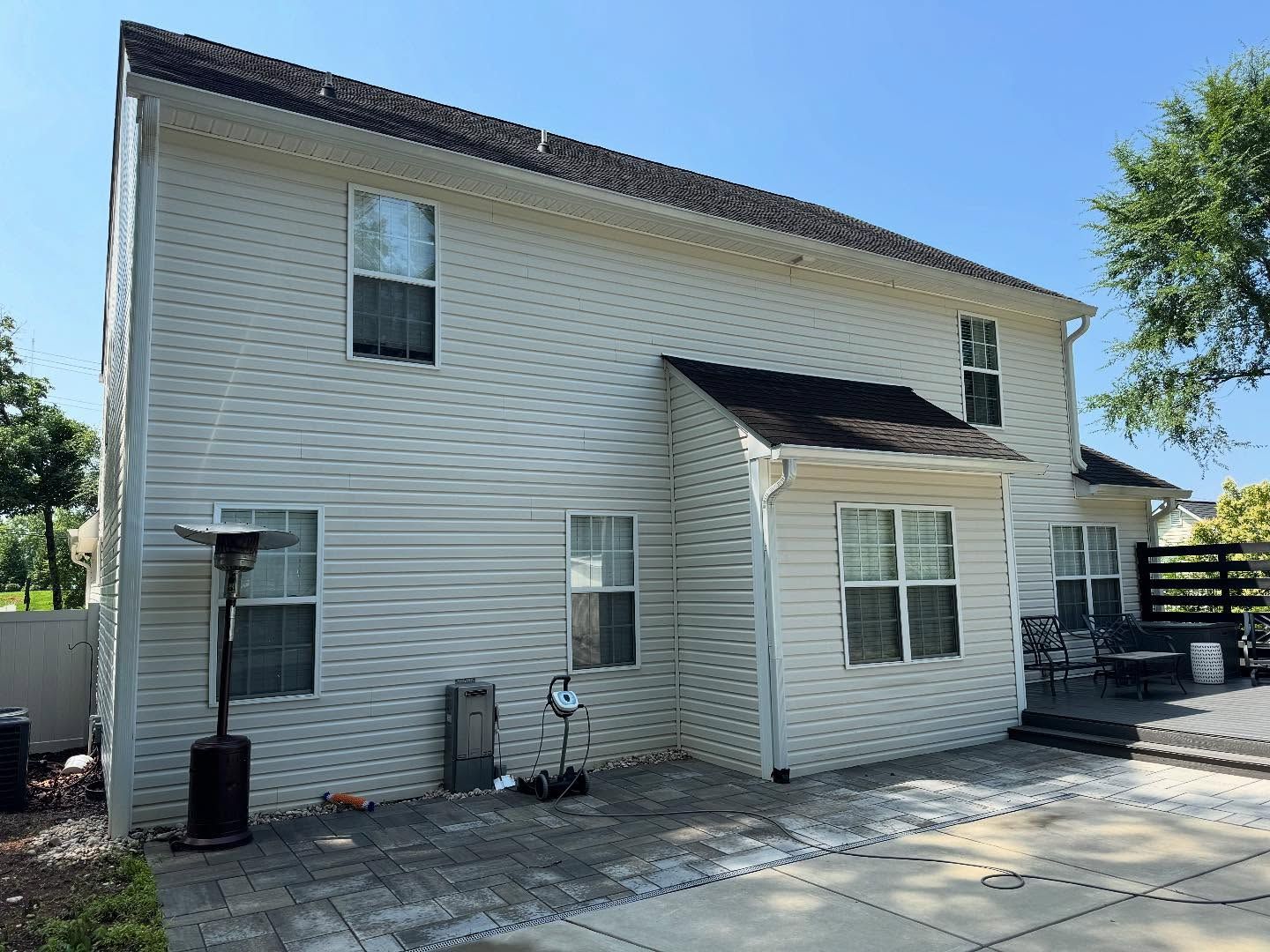 Back view of a two-story white house with dark roof, patio, and an outdoor heater.