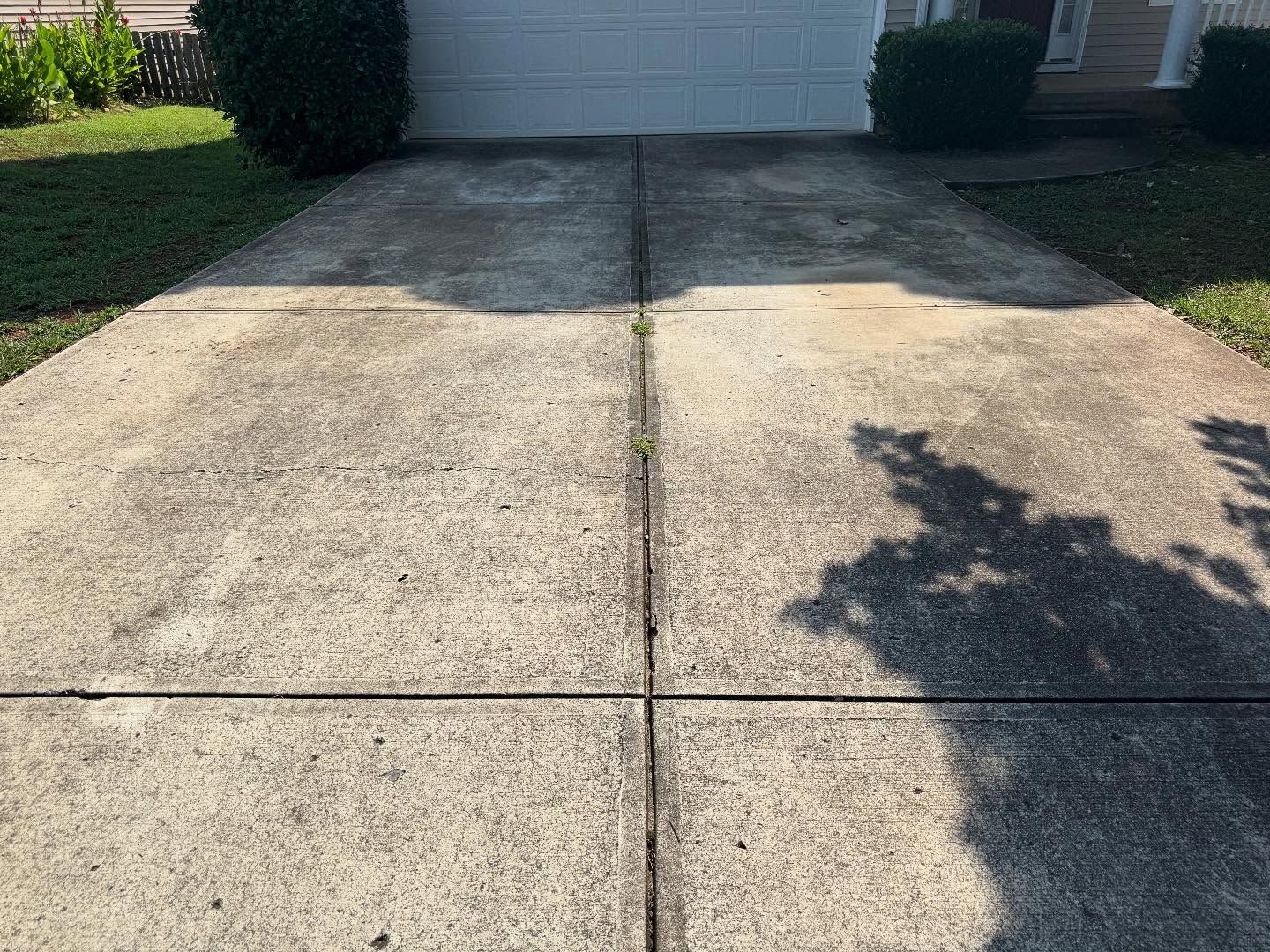 Concrete driveway with visible seams, shadow on the right, and patches of discoloration leading to a closed garage.