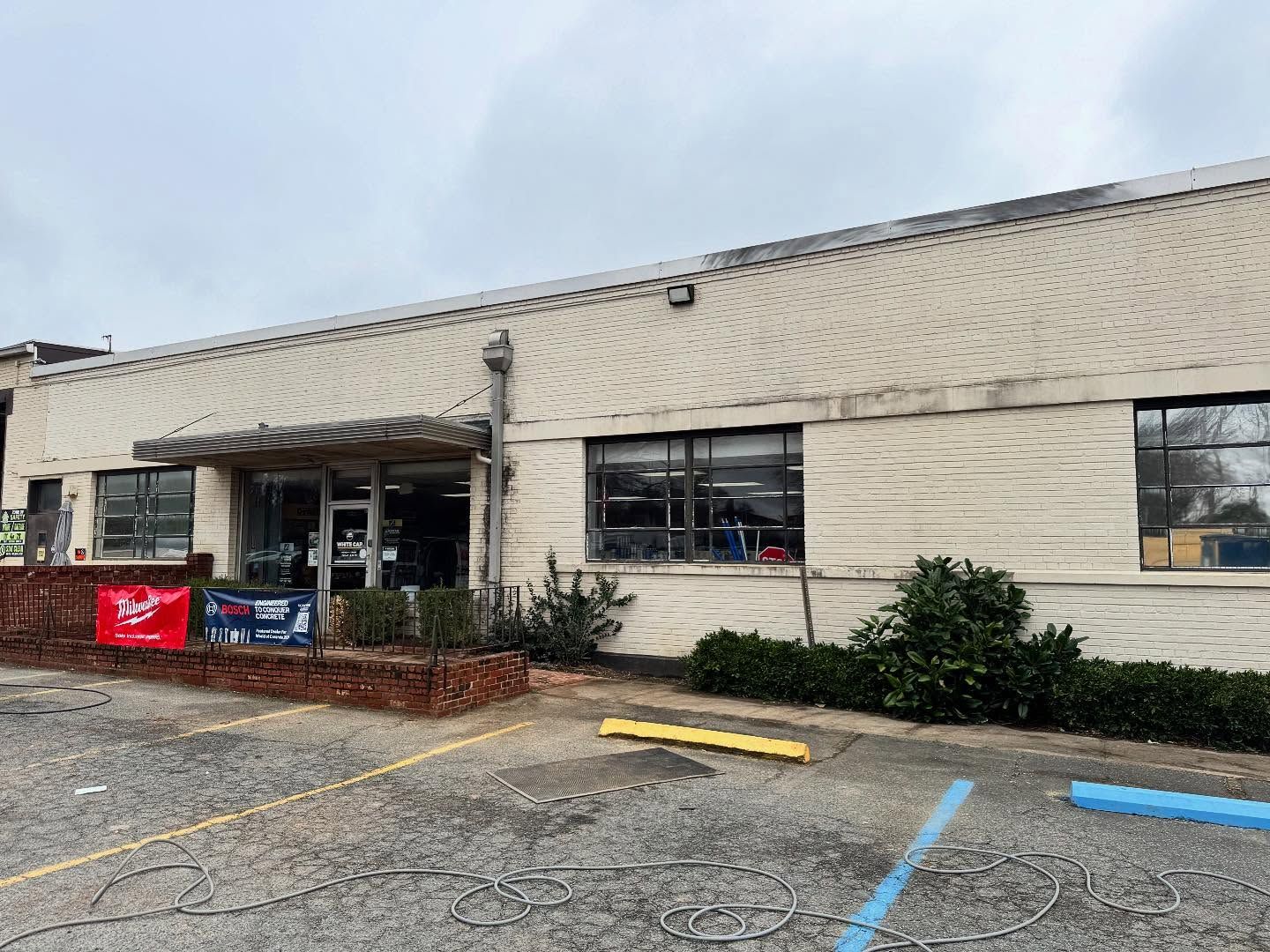 A building with a brick facade and multiple windows. A brick planter and a couple of banners are in front.