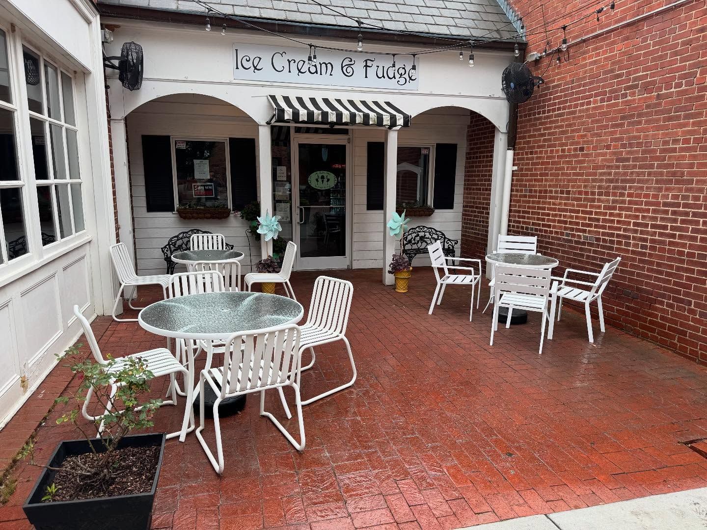 An ice cream and fudge shop with outdoor seating on a brick patio. White tables and chairs are set up in front of the shop.