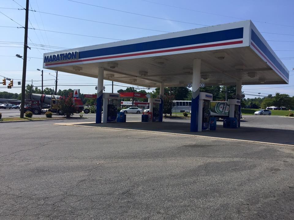 Marathon gas station with a blue and white canopy. Cars are parked at the pumps on a sunny day.