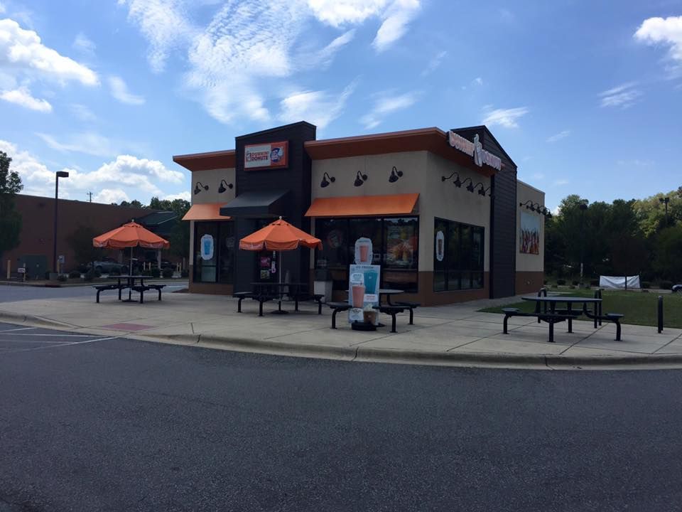 Exterior of a Dunkin' restaurant with orange accents, picnic tables, and umbrellas on a sunny day.