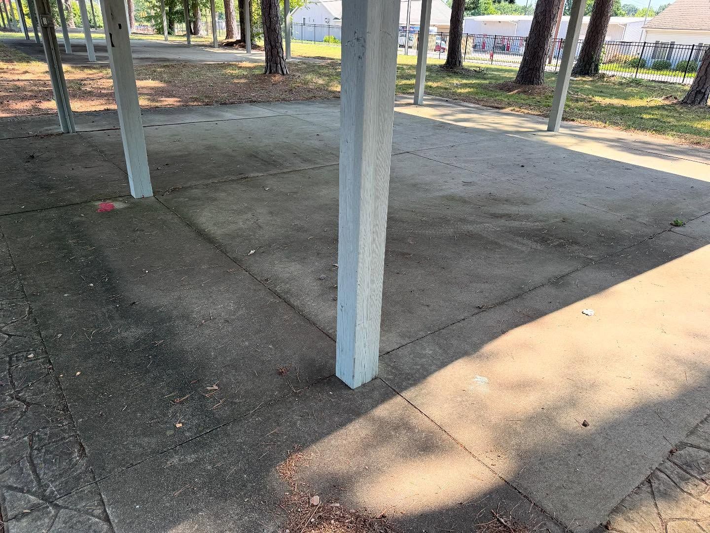 Concrete pavilion with light-colored square columns and floor. Sunny day, casting shadows.