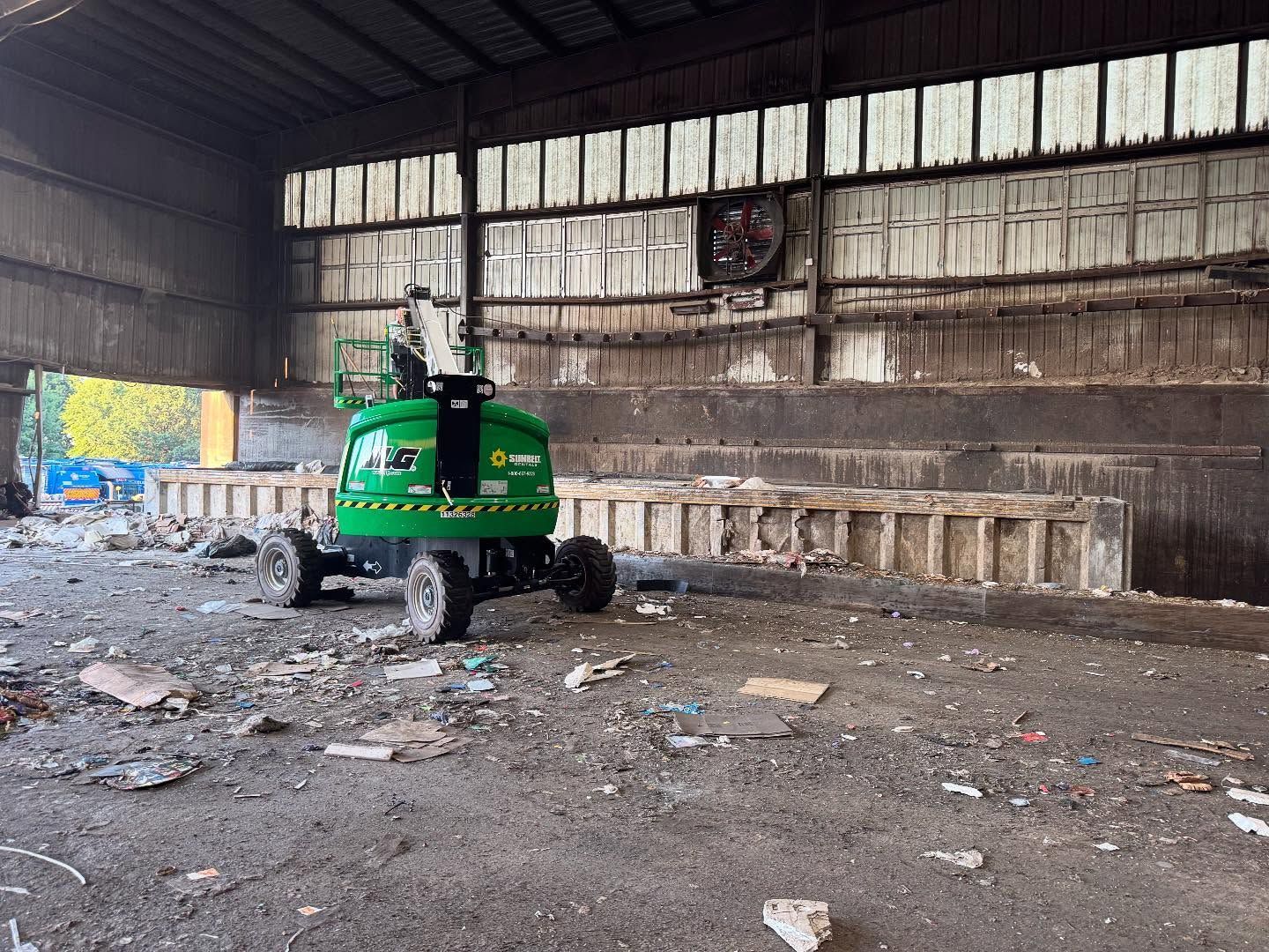 A green lift inside a dilapidated warehouse with exposed concrete and debris on the floor.