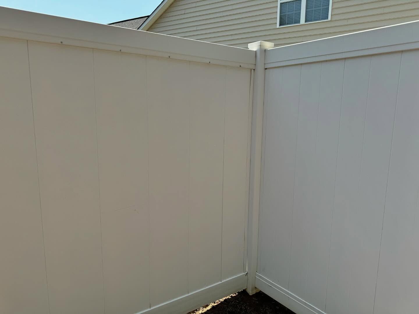 Beige vinyl fence corner; outdoors, with siding of a house visible above the fence.