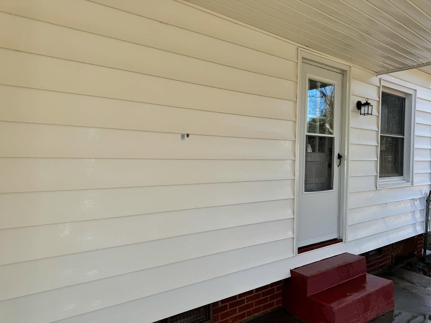 Exterior of a house with white siding, a white door with glass, and a small set of red steps.