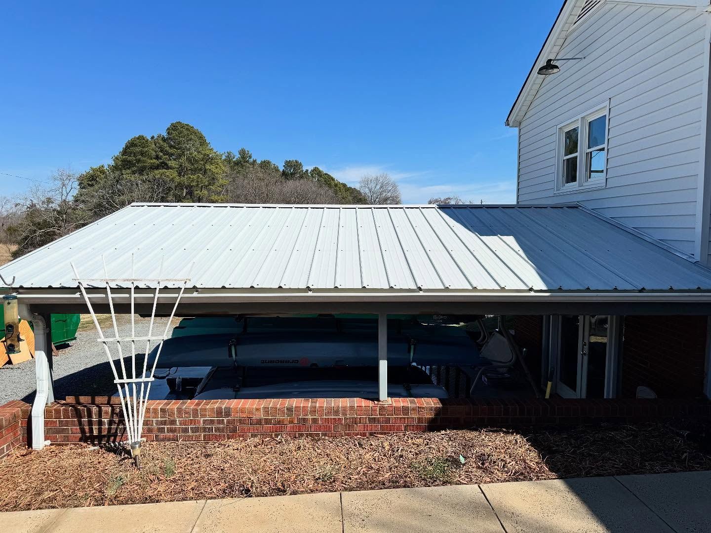 White metal roof extending from a two-story building, covering a space with kayaks, against a clear blue sky.