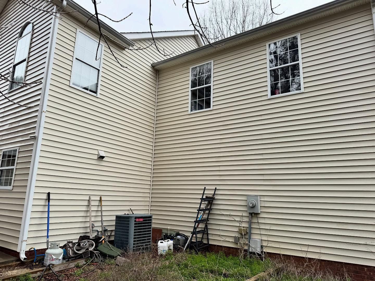 A beige two-story house with vinyl siding. There is an air conditioning unit, ladder, and electrical box.
