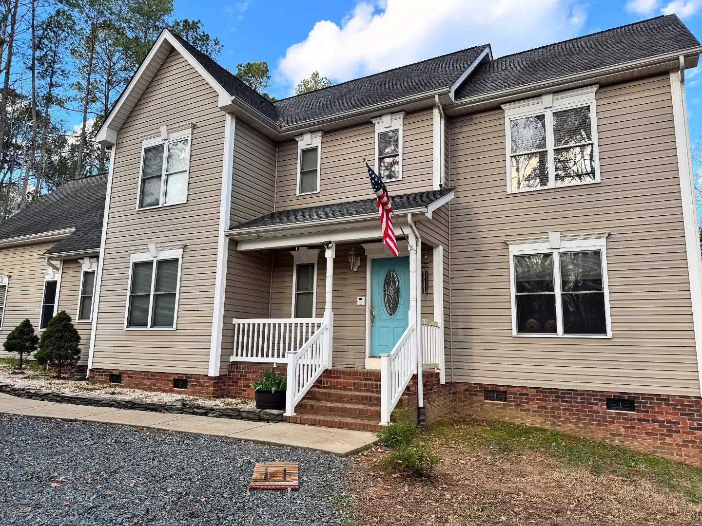 Beige two-story house with a blue front door and a small porch. An American flag hangs beside the door.