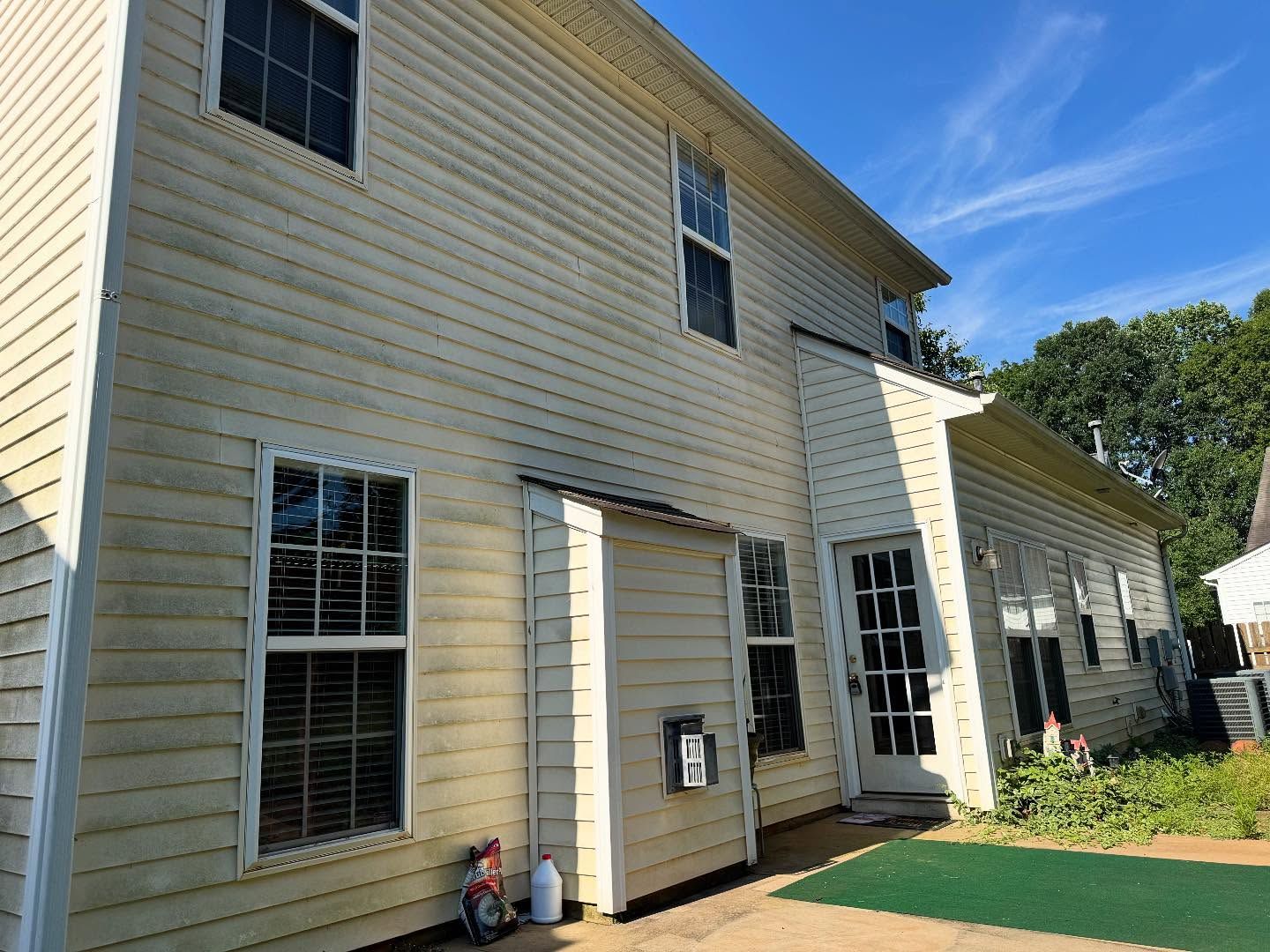 Side of a two-story house with light siding and multiple windows under a blue sky.