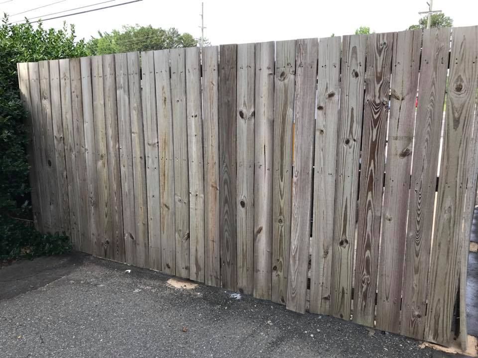 Wooden fence in an outdoor setting; weathered and gray, with some greenery visible to the left.