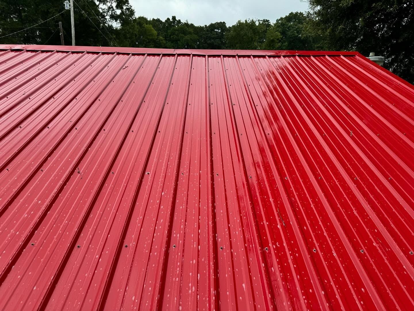 Red metal roof with vertical ridges, reflecting light; against a background of trees and sky.