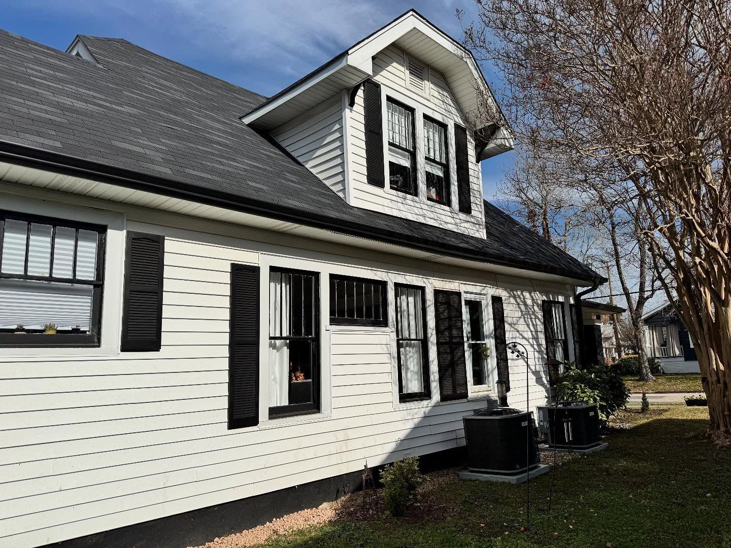 White house with black shutters and a dark gray roof under a partly cloudy sky.
