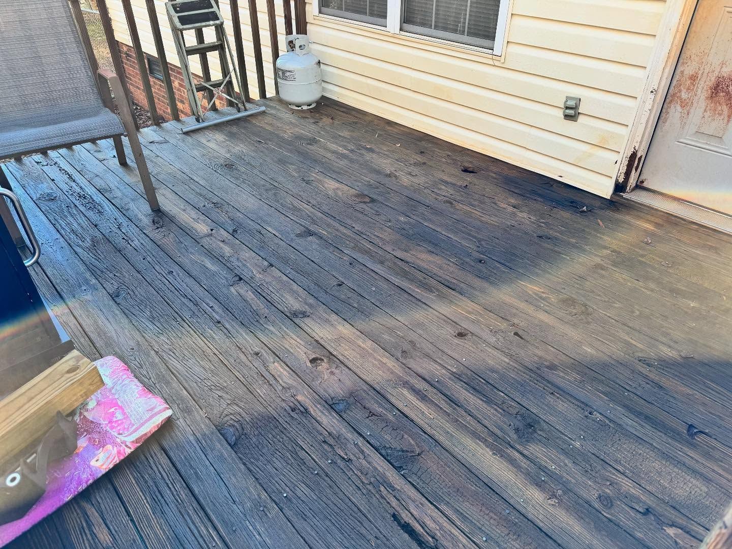 Wooden deck with a chair, propane tank, and a door, sunlight casting long shadows.