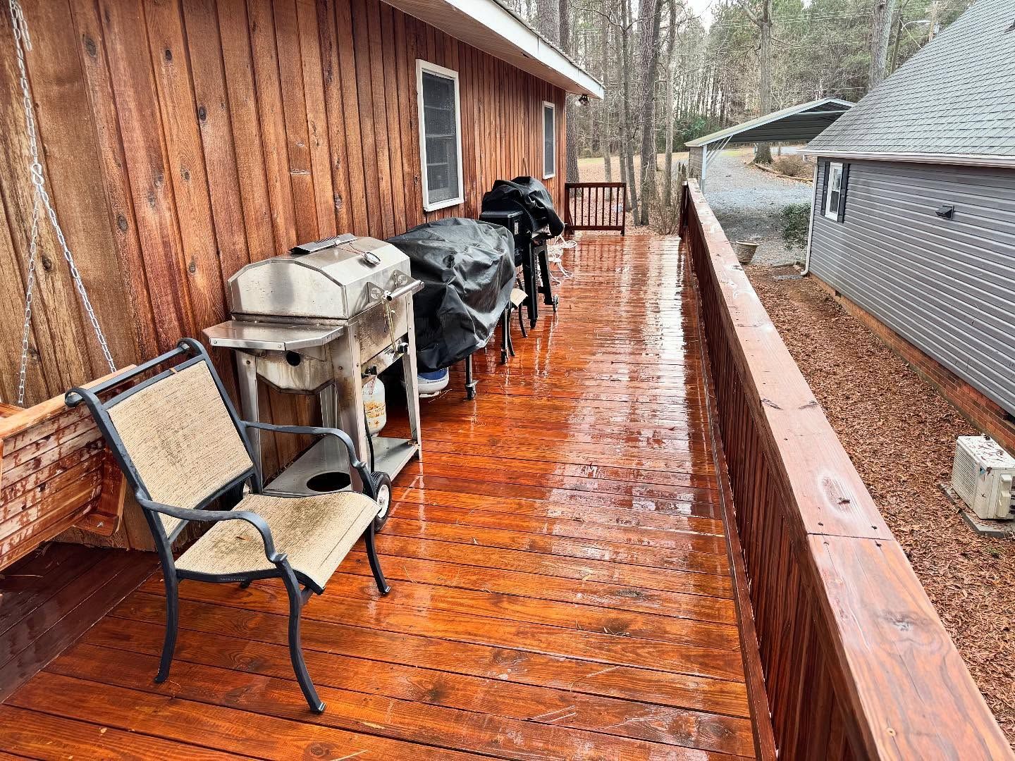 Wooden deck with brown chairs, a grill, and covered grills. A building with a wooden exterior is in the background.