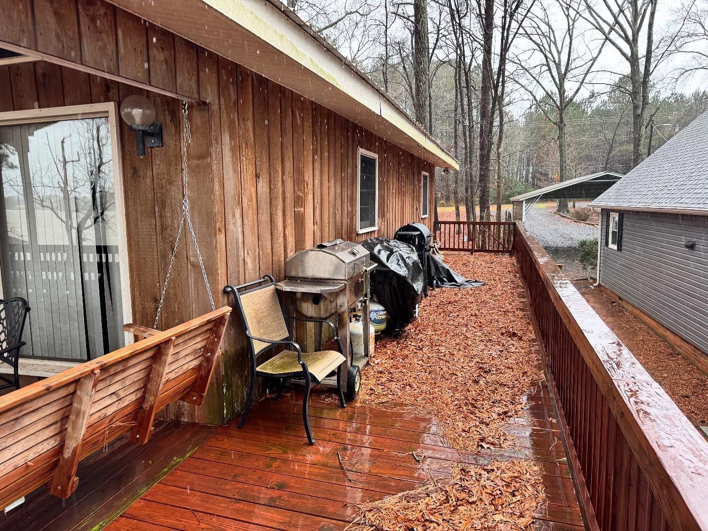 Wooden deck covered in fallen leaves with a grill, chairs, and covered 
