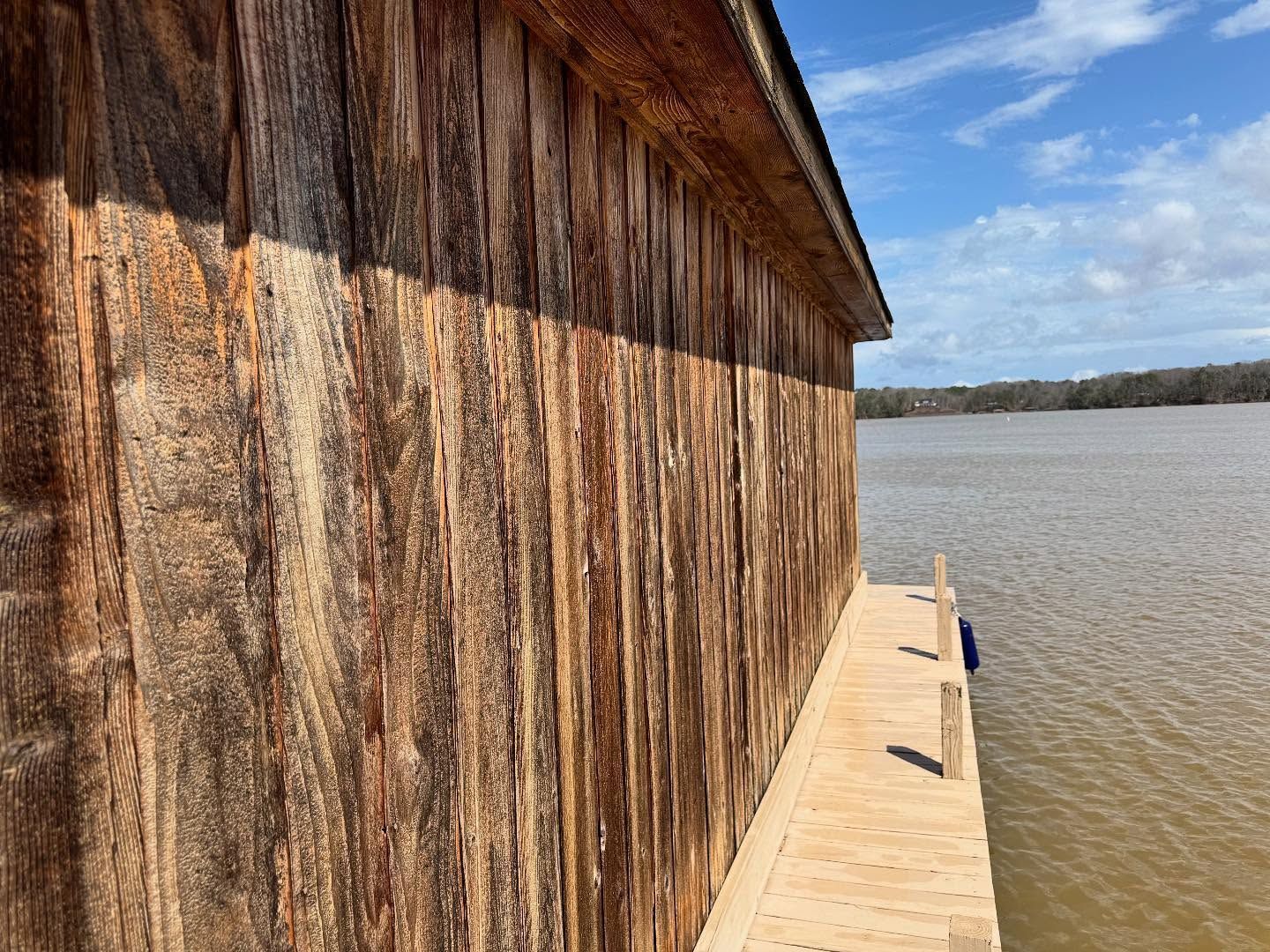 Weathered wooden building by a body of water under a blue sky. A small wooden dock is attached to the building.