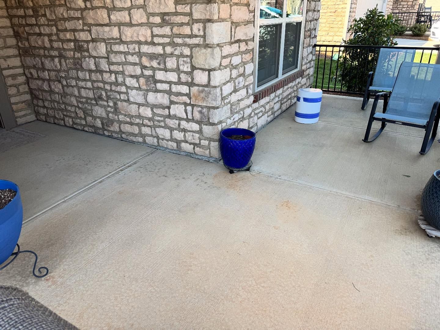 A patio with stone brick walls, concrete flooring, and blue planters. Blue rocking chairs are also on the patio.