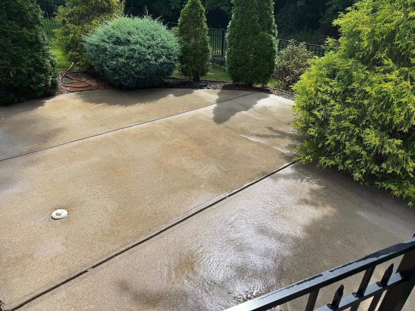 Covered concrete patio with support beams, some water puddles, and a view of trees and water in the background.