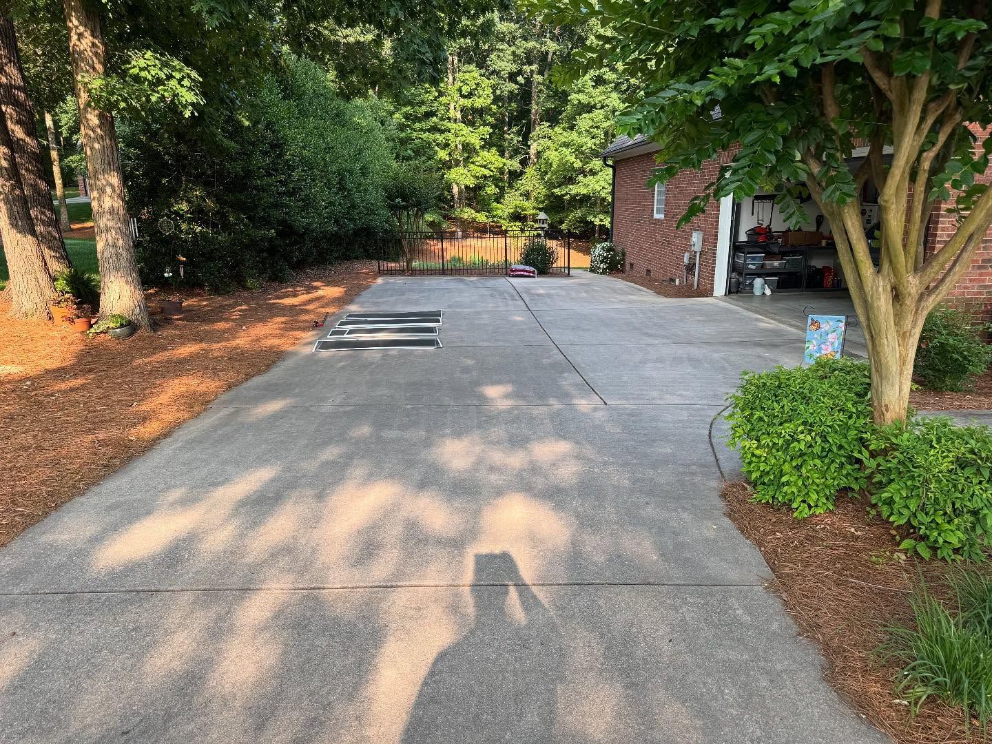 A concrete driveway leading to a brick house with a garage. A tree casts a shadow on the driveway.
