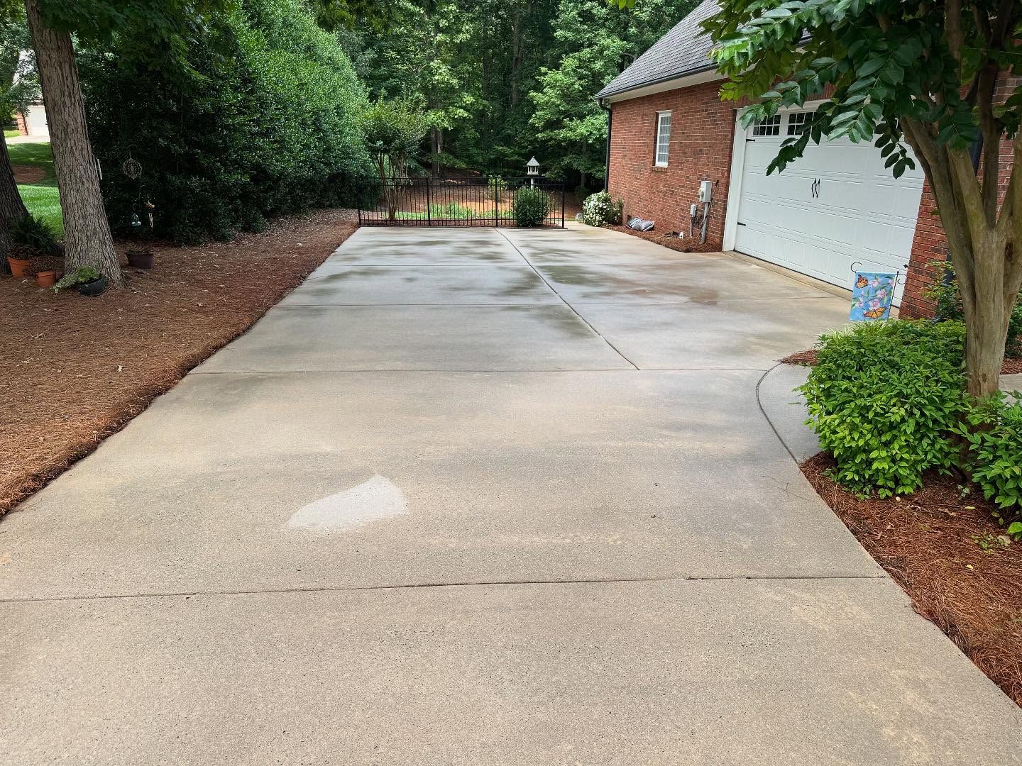 Driveway leading to a garage, with brown mulch bordering the edges. The driveway is concrete and wet.