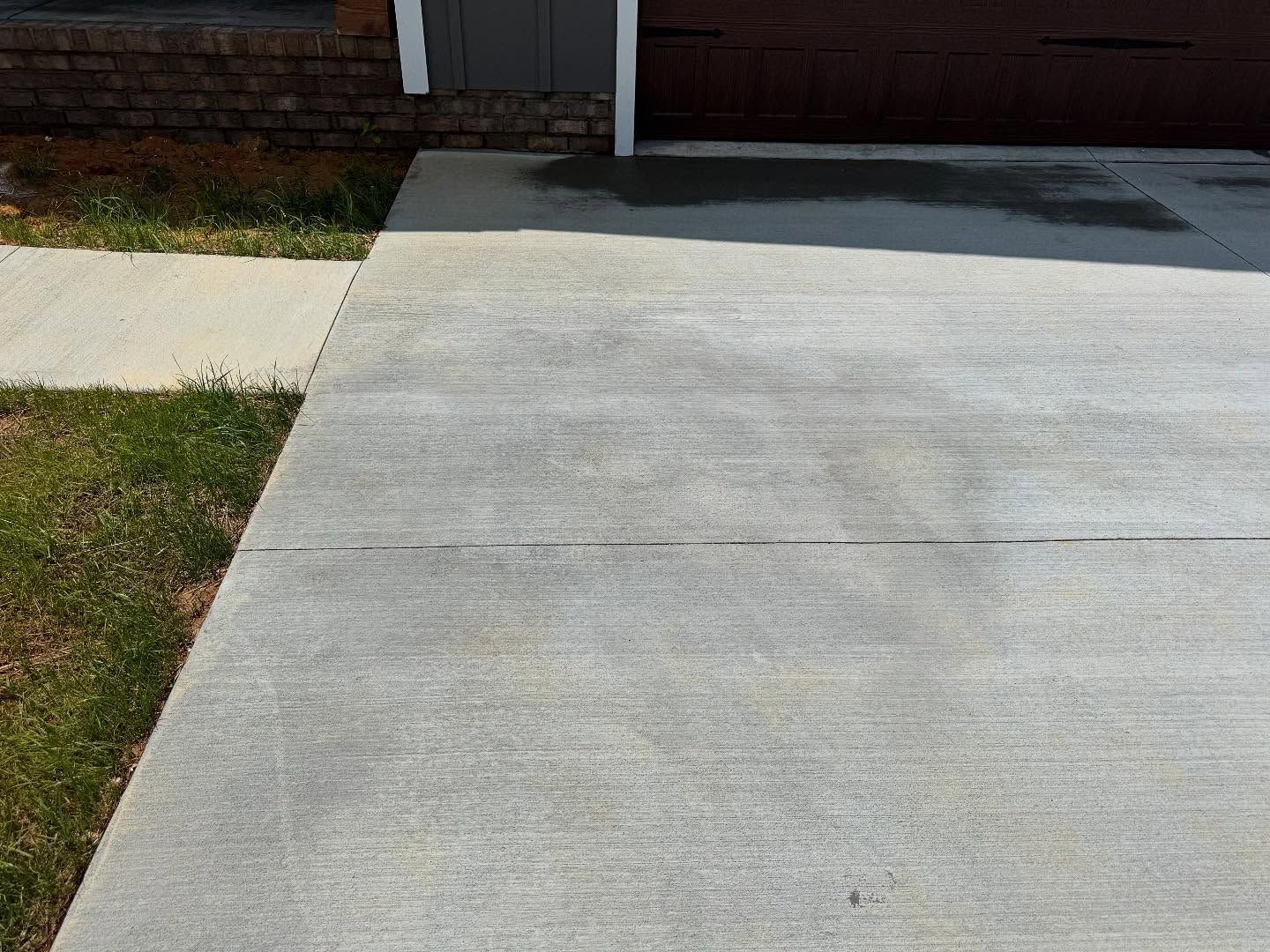 Concrete driveway and sidewalk next to a grassy area and brick wall. There is a small amount of wetness on the concrete.