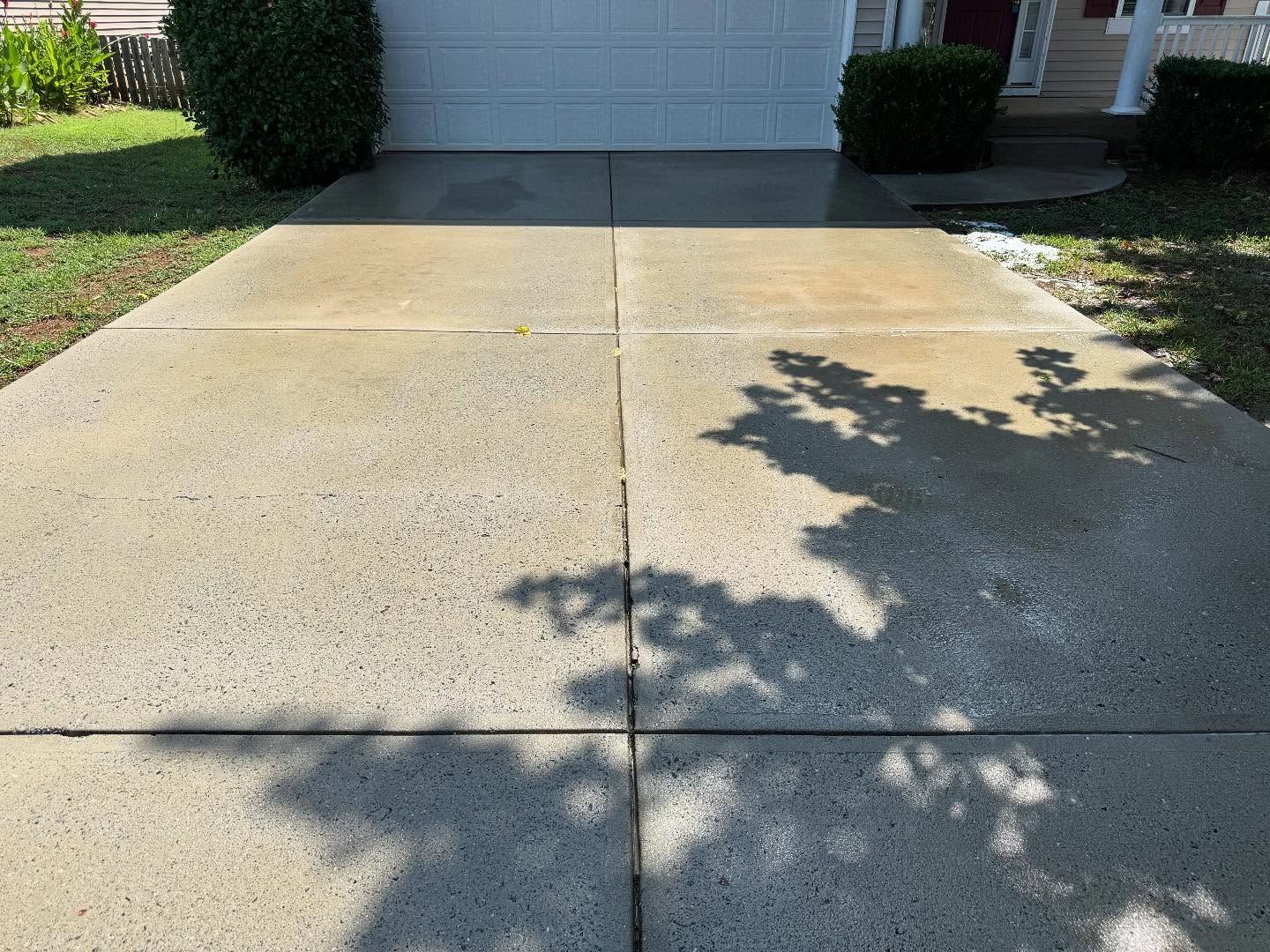 Concrete driveway in front of a house, with shadows from a tree. The driveway has four large square sections.