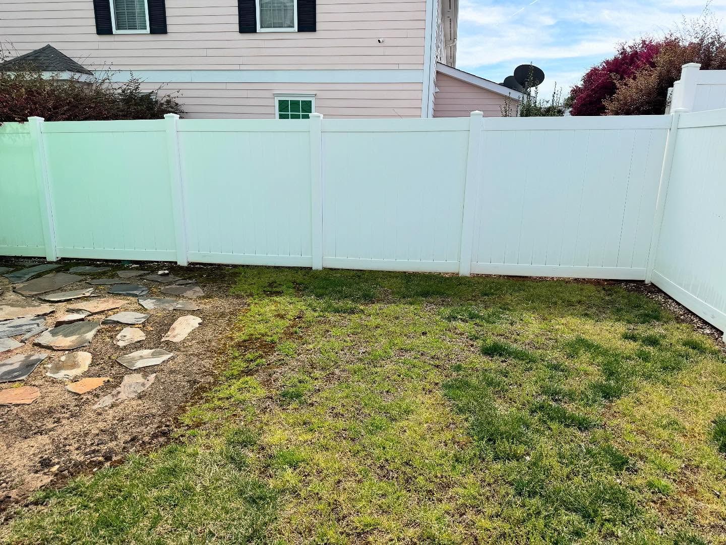White fence encloses a grassy yard with stone pathway; a two-story house is in the background.