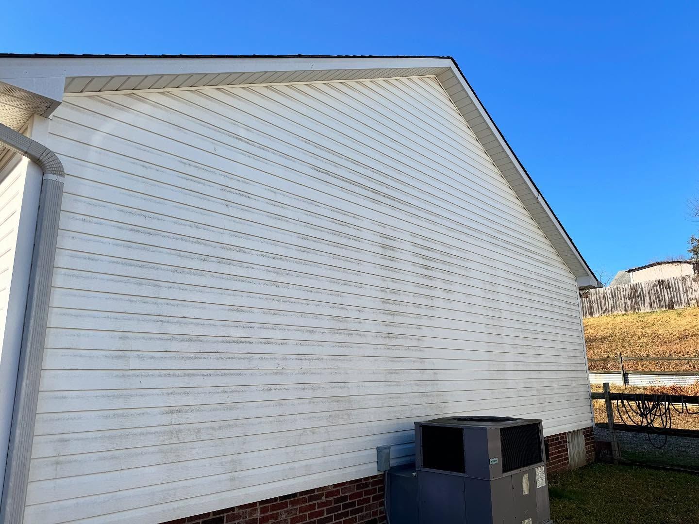 Side of a white house with dirty siding, an AC unit, and a clear blue sky.