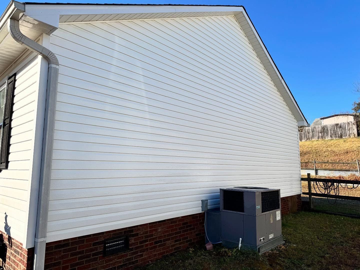 White vinyl-sided house with brick foundation, featuring an air conditioning unit on the lawn under a blue sky.