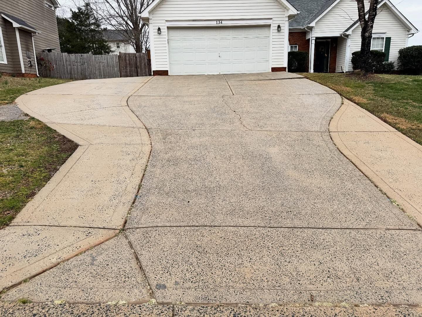Driveway leading to a house with a white garage door. The driveway is concrete with grass on either side.