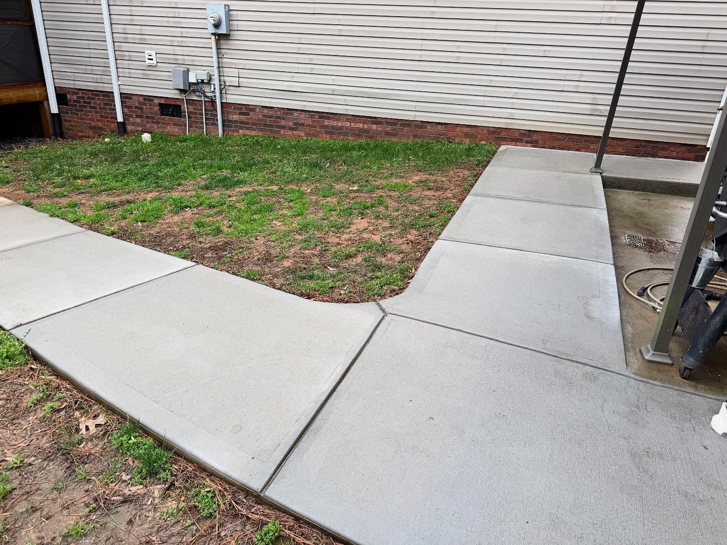 Concrete sidewalk extending in two directions through a grassy yard, adjacent to a building's siding.
