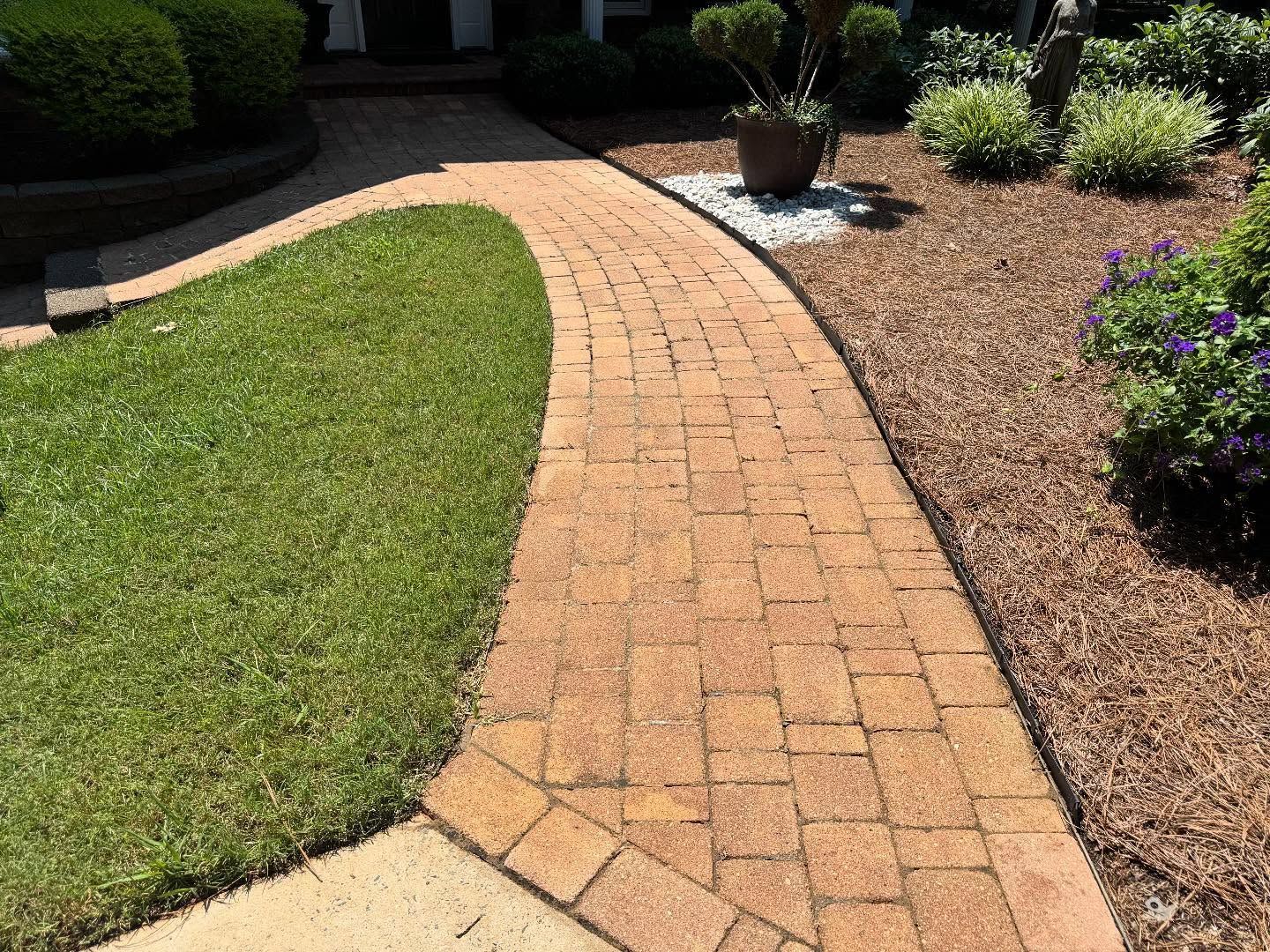 Brick walkway winding through a landscaped yard with green grass and brown mulch.