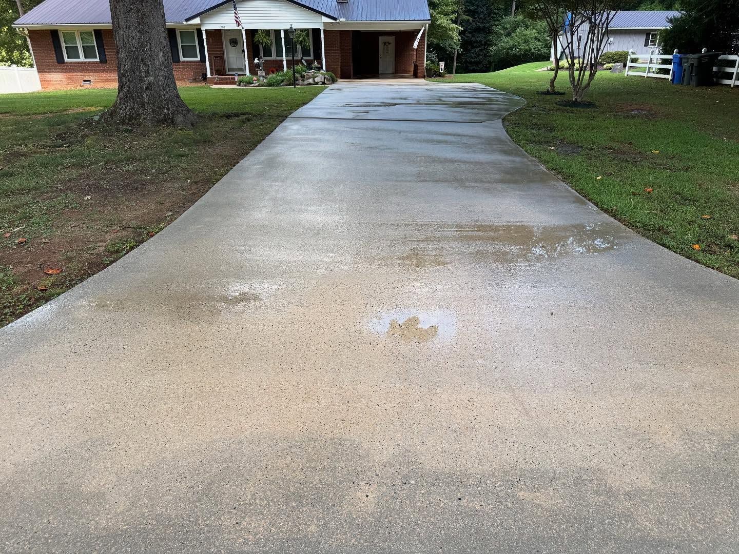 A concrete driveway leads to a house with a brick facade. Patches of water and