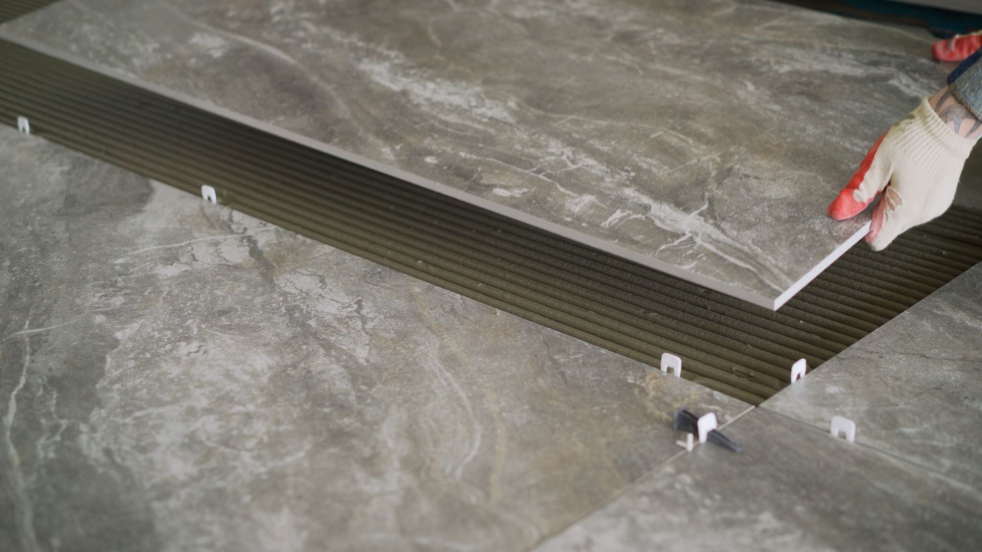Construction workers laying tile over concrete floor using tile levelers, notched trowels and tile mortar.