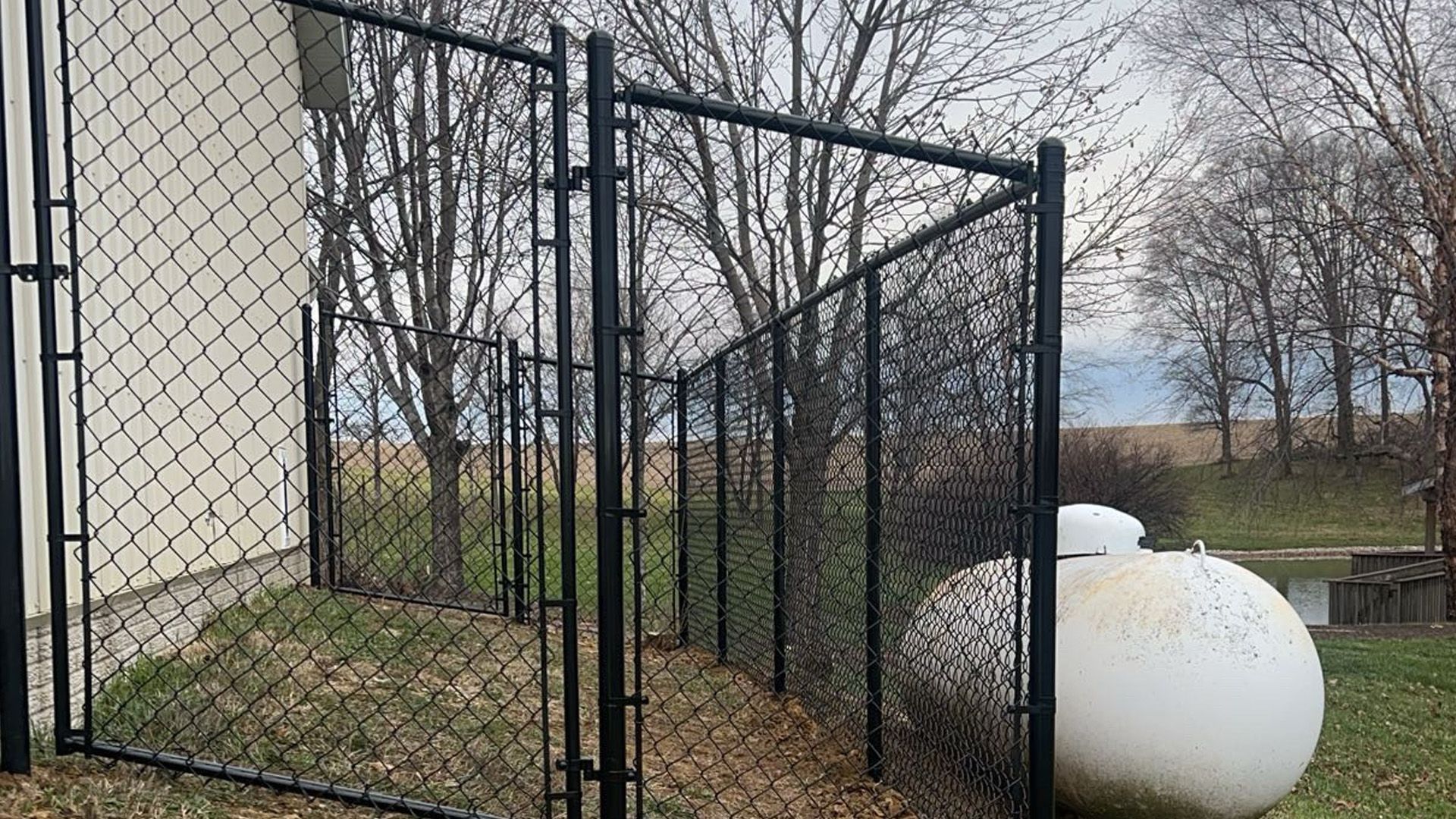 A propane tank is behind a chain link fence.