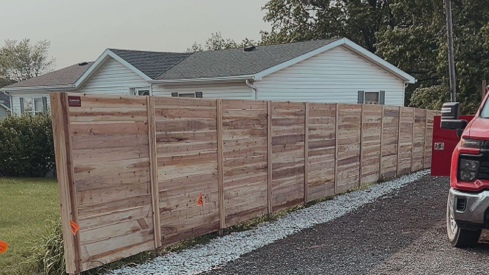 A red truck is parked next to a wooden fence in front of a house.