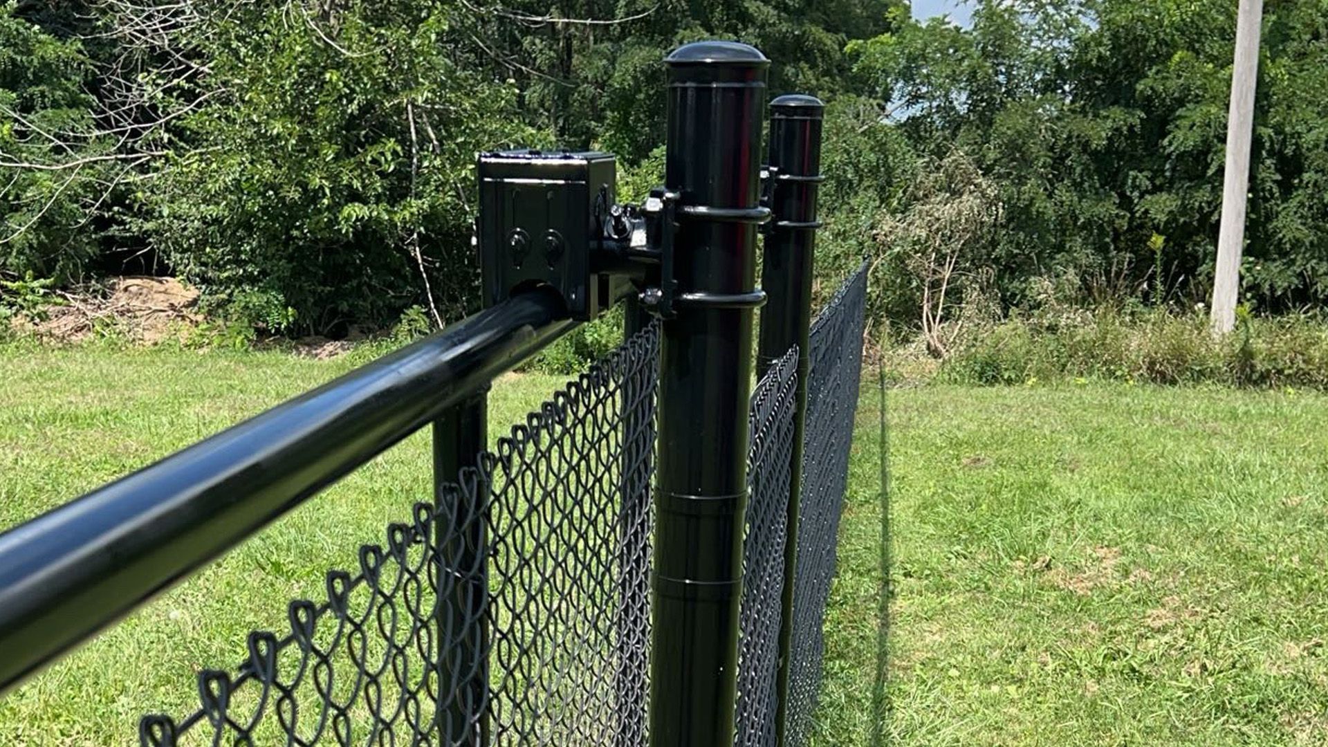 A black chain link fence is sitting in the middle of a grassy field.