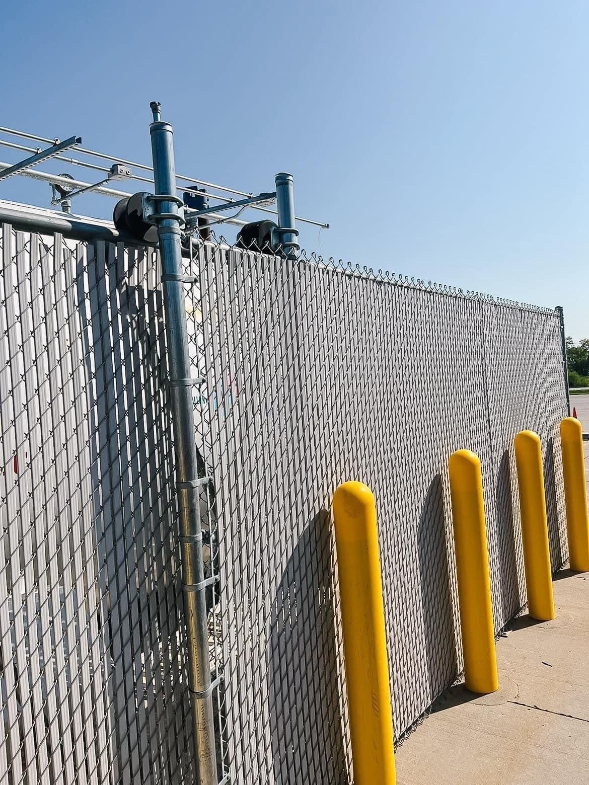 A chain link fence with yellow poles along the sidewalk
