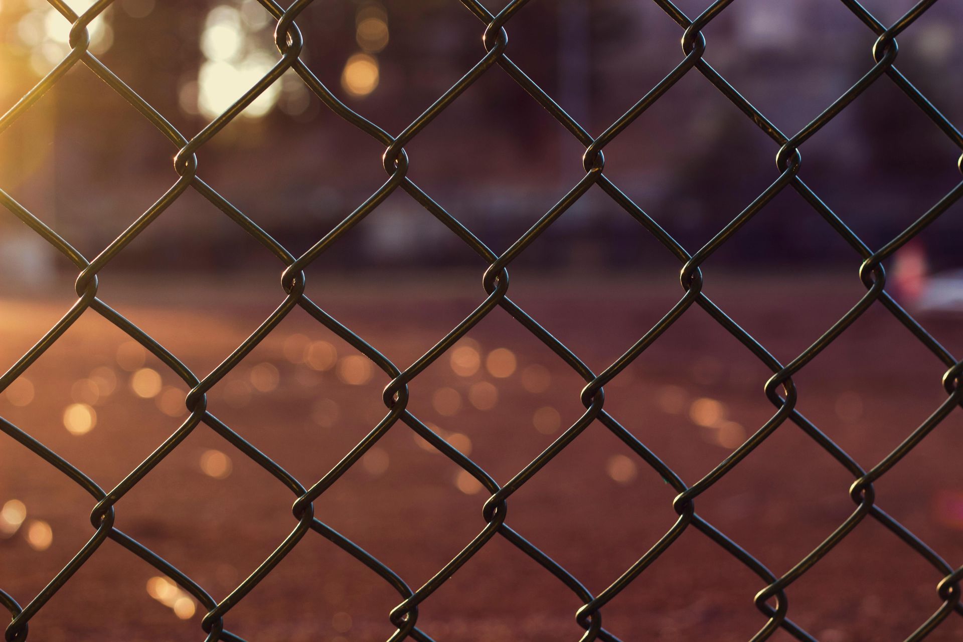 A close up of a chain link fence with a tennis court in the background.