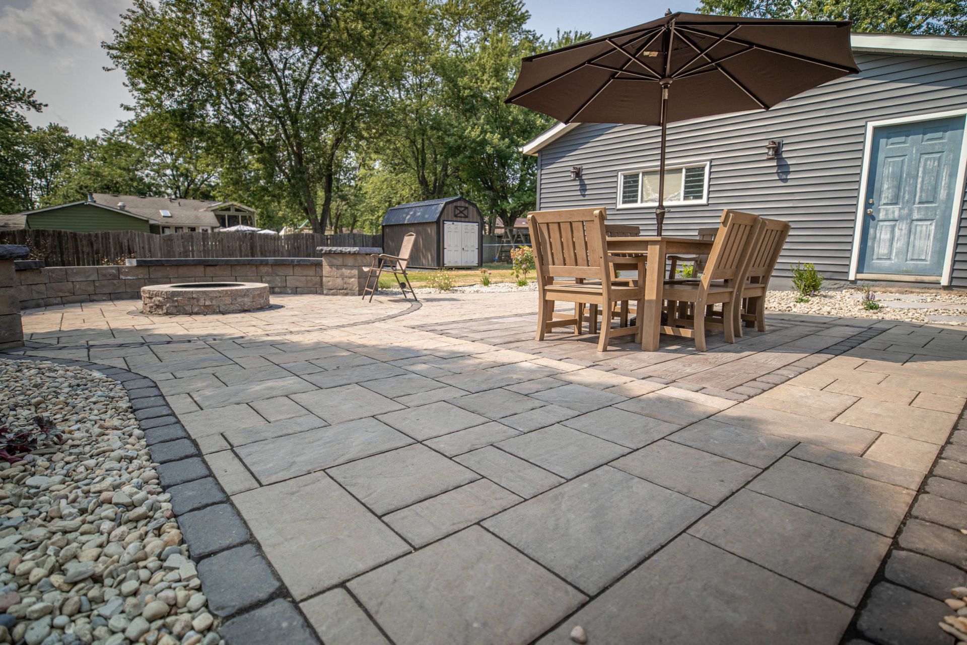 A brick paver patio with a table and chairs and an umbrella in front of a house.