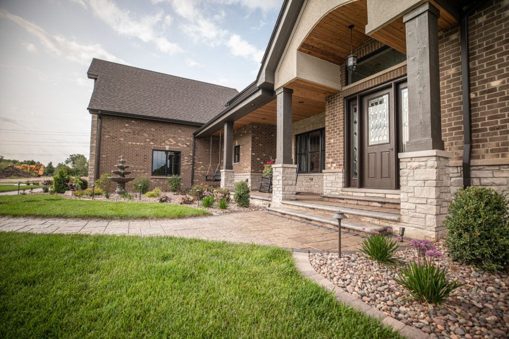 A large brick house with a large porch and steps is sitting on top of a lush green lawn.