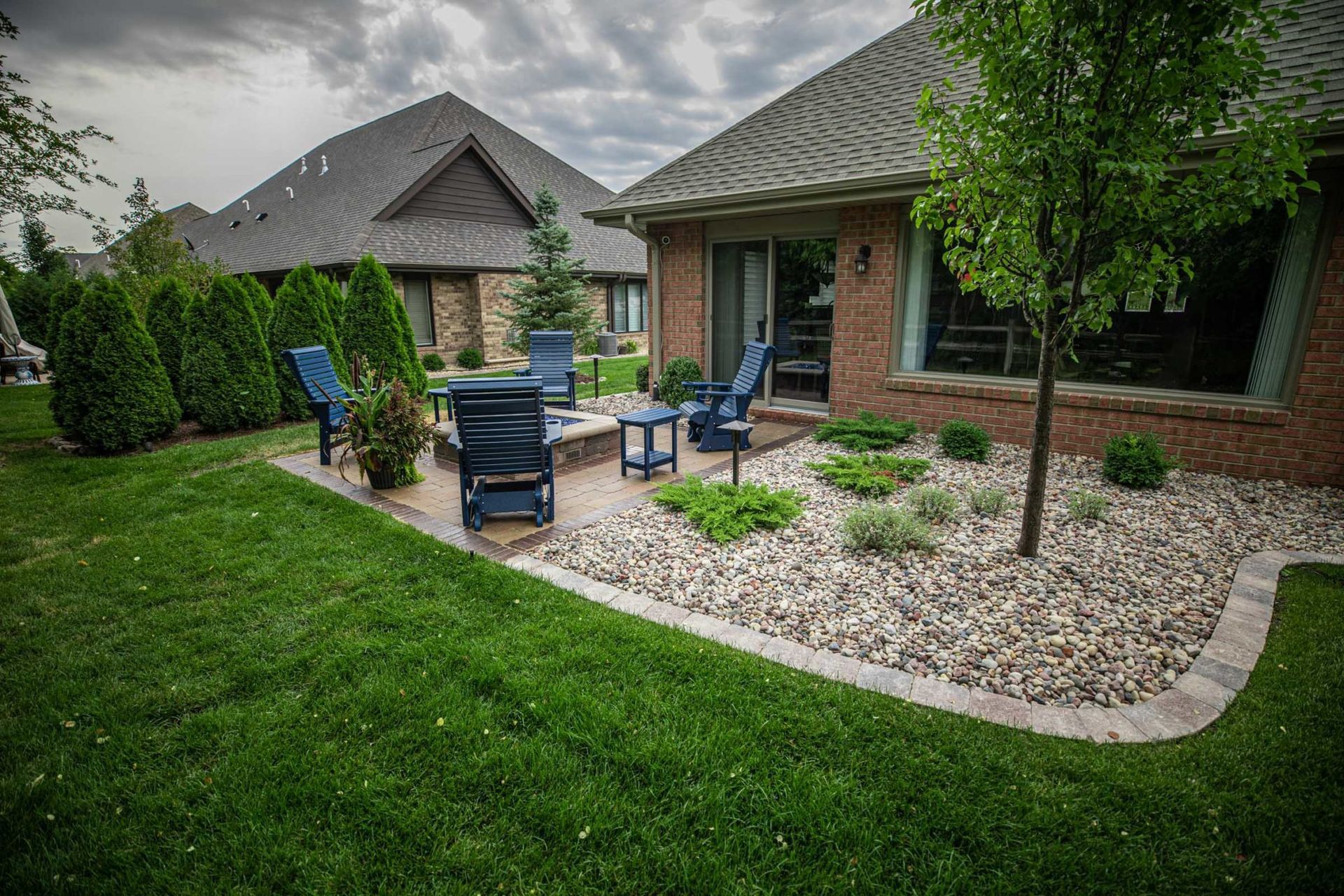A backyard with a patio and chairs in front of a brick house.