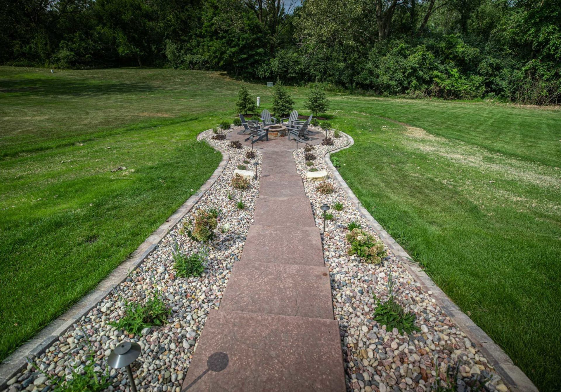 A stone walkway leading to a fire pit in the middle of a lush green field.